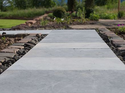 Modrokamenné desky jako zahradní cesta se záhony květin a zeleným trávníkem v pozadí