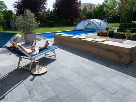 Žena odpočívá na lehátku na terase s vápencovými deskami, v pozadí zahrada s bazénem