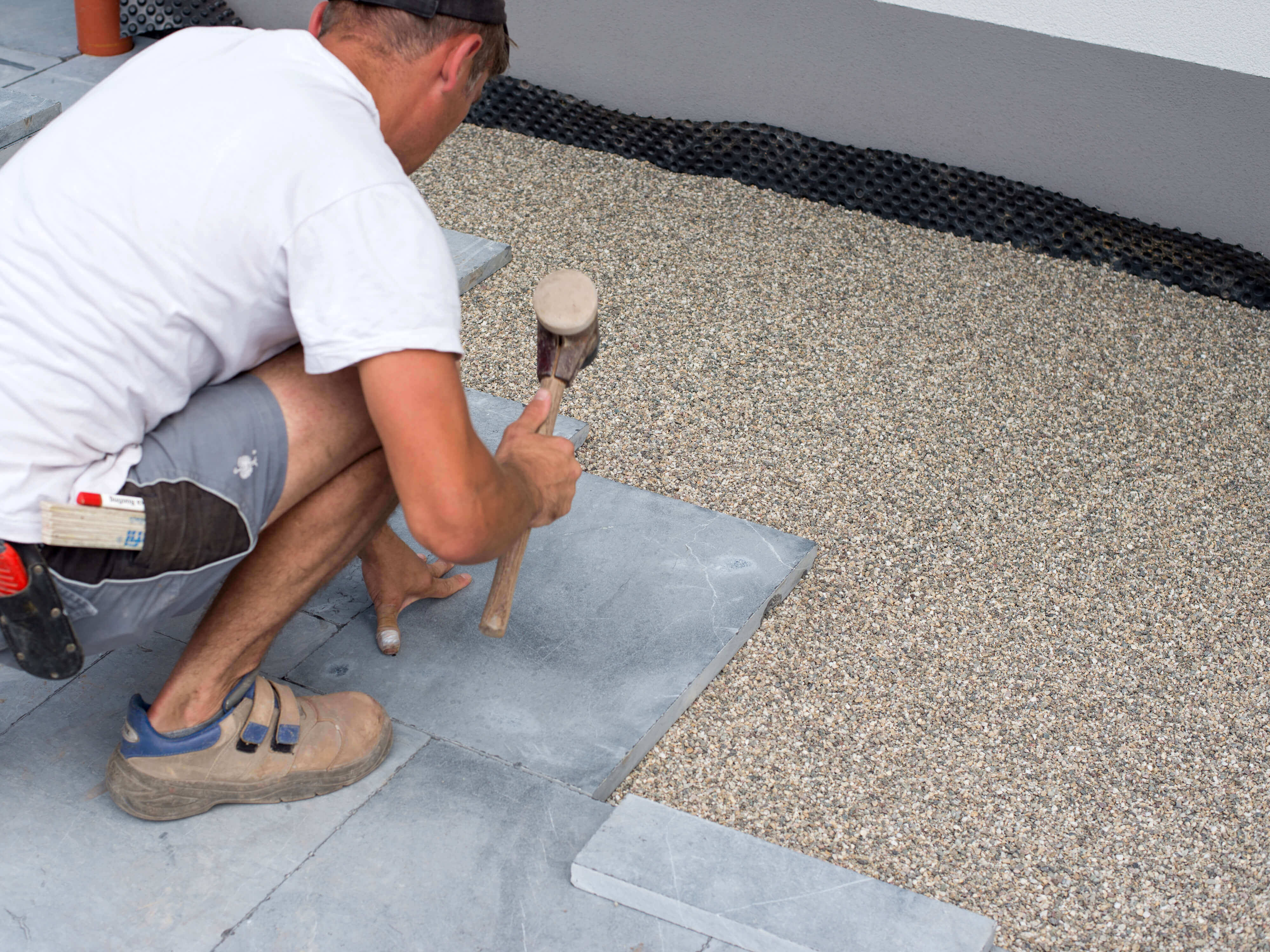 Muž pokládá modrokamenné desky do lože ze štěpky