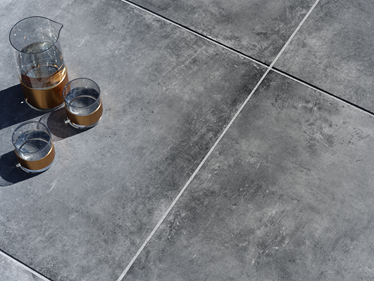 Tmavá betonová terasová deska Vulkano s karafou a sklenicemi