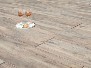 Dvě sklenice na víno a květina na terasových dlaždicích s efektem dřeva