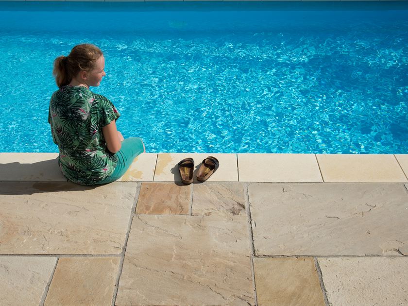 Dívka sedící u modrého bazénu s pískovcovými deskami Yellow Mint