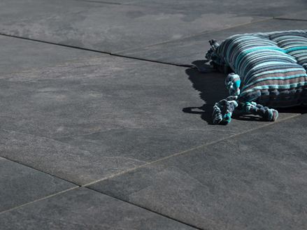 Polštář leží na tmavě šedé kameninové dlažbě Alpine Black