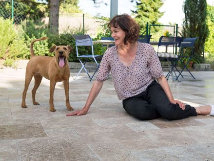 Žena sedící na terase s hnědými travertinovými deskami, vedle ní pes