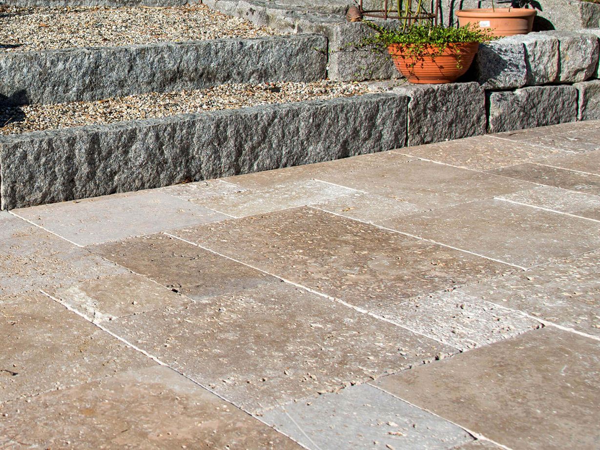 Terasa s přírodními kamennými deskami z hnědého travertinu, v pozadí schodiště s žulovými kameny