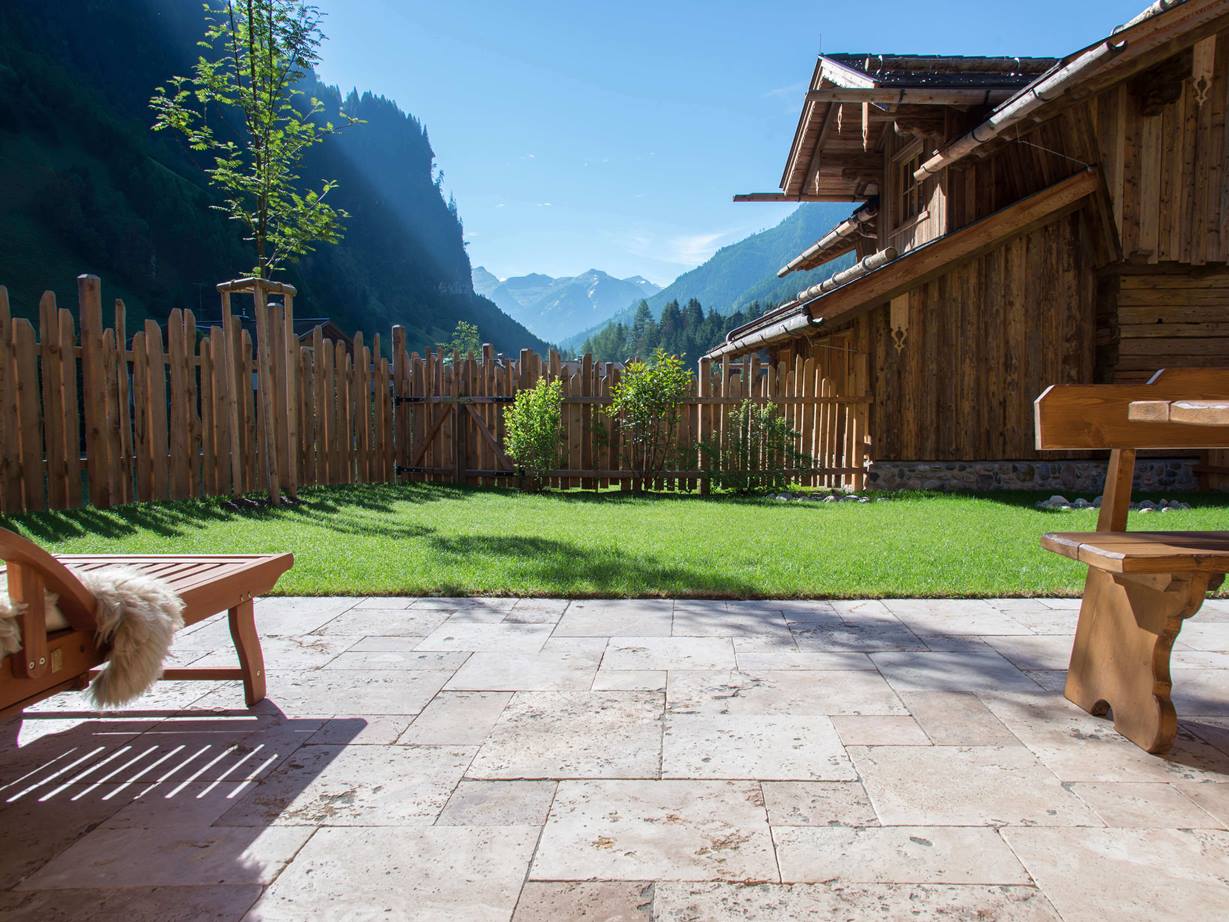 Podlaha terasy s travertinovým Rustic a dřevěným nábytkem, trávník v pozadí a výhled na hory