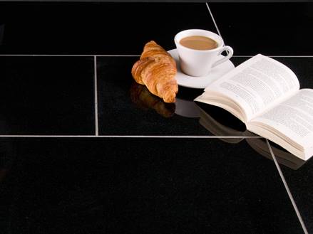 Šálek kávy, croissant a otevřená kniha na tmavé žulové dlažbě se světlou spárovací hmotou