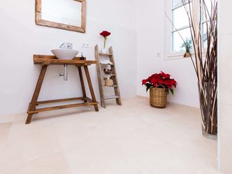 Koupelna s dřevěným nábytkem a světlými dlaždicemi z přírodního vápence jako podlahou