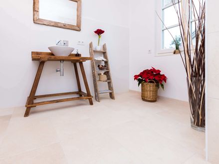 Koupelna s dřevěným nábytkem a světlými dlaždicemi z přírodního vápence jako podlahou