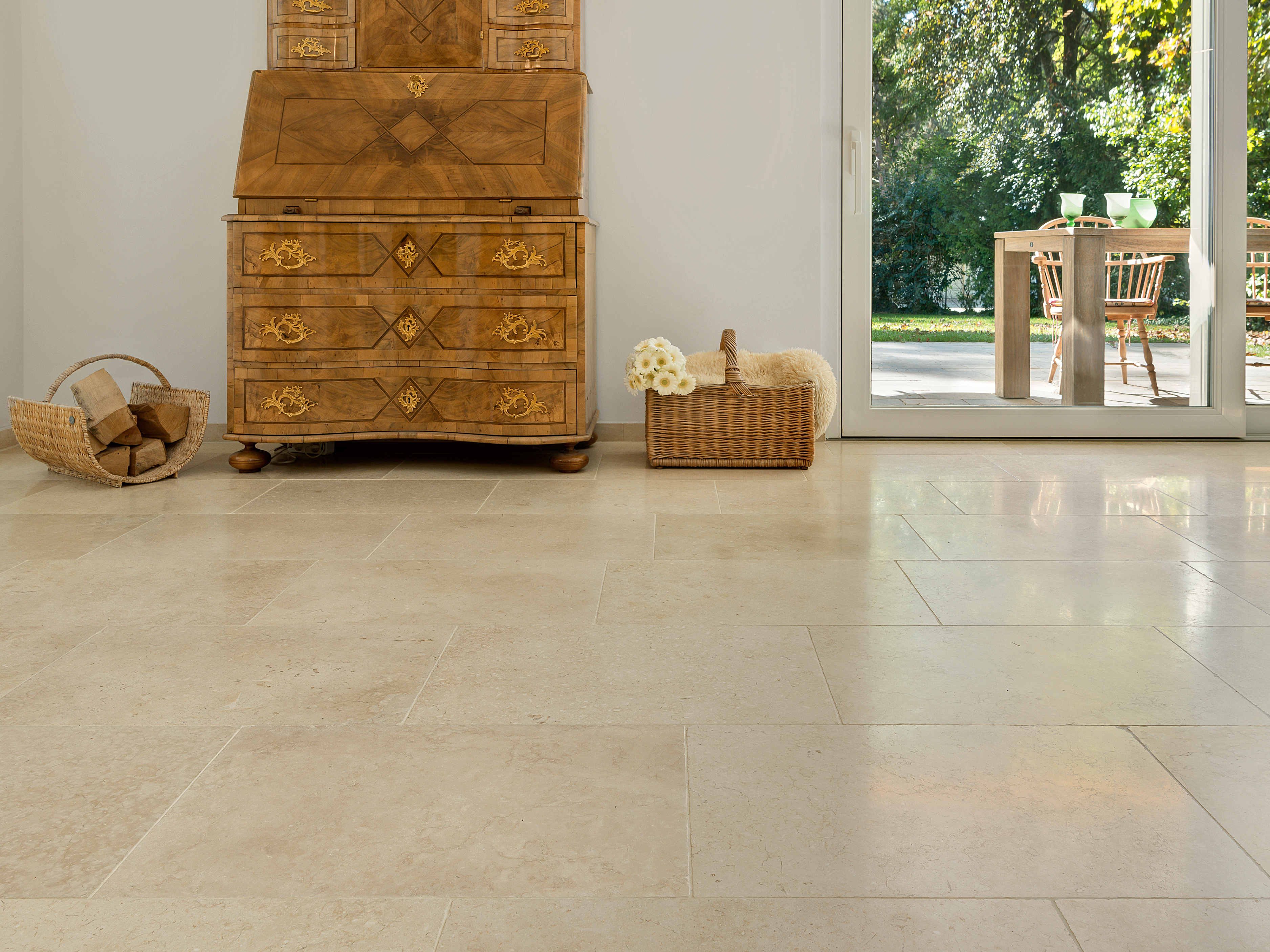 Harmonické béžové tóny: vápencová dlažba Cleopatra Light Starožitná dřevěná skříň na světlých vápencových dlaždicích Cleopatra Light, v pozadí pohled na terasu a zahradu