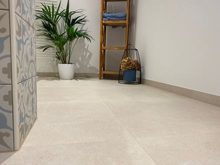 Moderní koupelna s dřevěným nábytkem, dekorativní rostlinou a světlými obklady ve vzhledu vápence