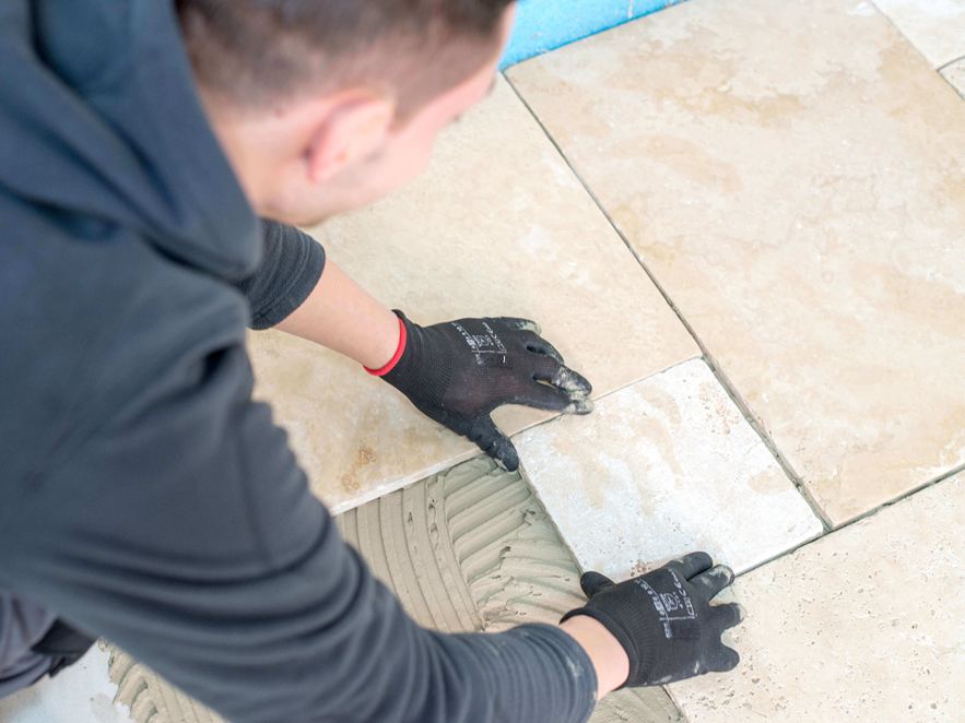 Muž pokládá travertinové dlaždice světle béžové barvy v římské vazbě