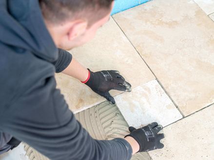 Muž pokládá travertinové dlaždice světle béžové barvy v římské vazbě