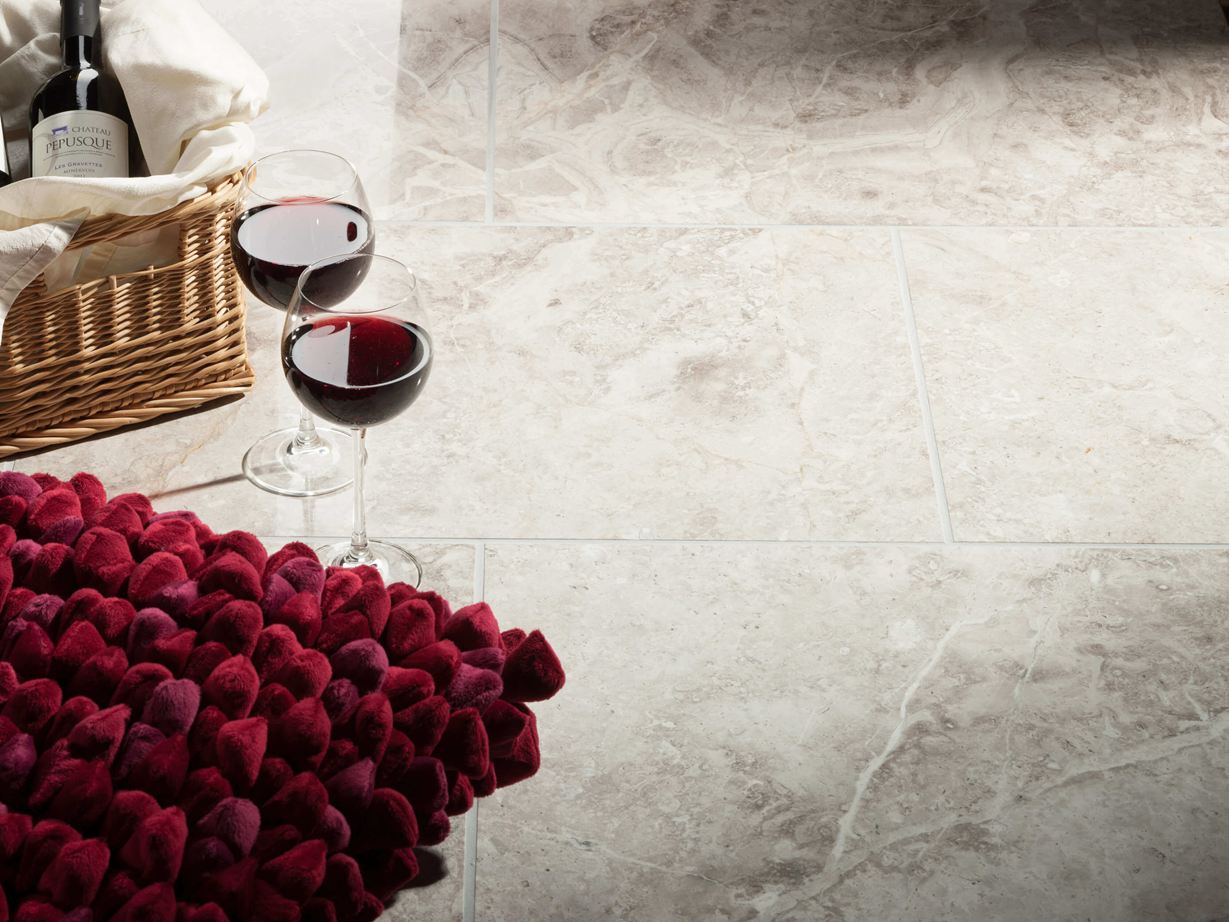Dvě sklenice na víno stojí vedle koše s lahví vína a červeným polštářkem na mramorových dlaždicích Silver Shadow.