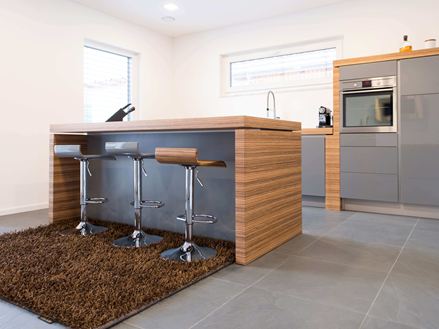 Kuchyně s otevřeným barovým pultem, moderními dřevěnými prvky a tmavou břidlicovou podlahou