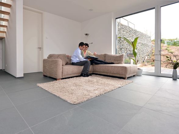 Velkoformátová břidlicová dlažba Grey Slate v obývacím pokoji se světlou pohovkou a bílými stěnami. Pár sedící na pohovce