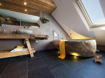 Rustikální koupelna s vanou ve vzhledu kamene a tmavými břidlicovými dlaždicemi jako podlahou