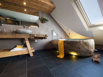 Rustikální koupelna s vanou ve vzhledu kamene a tmavými břidlicovými dlaždicemi jako podlahou