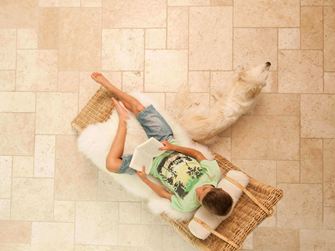 Chlapec si čte na lehátku na světlých travertinových dlaždicích položených v římské vazbě