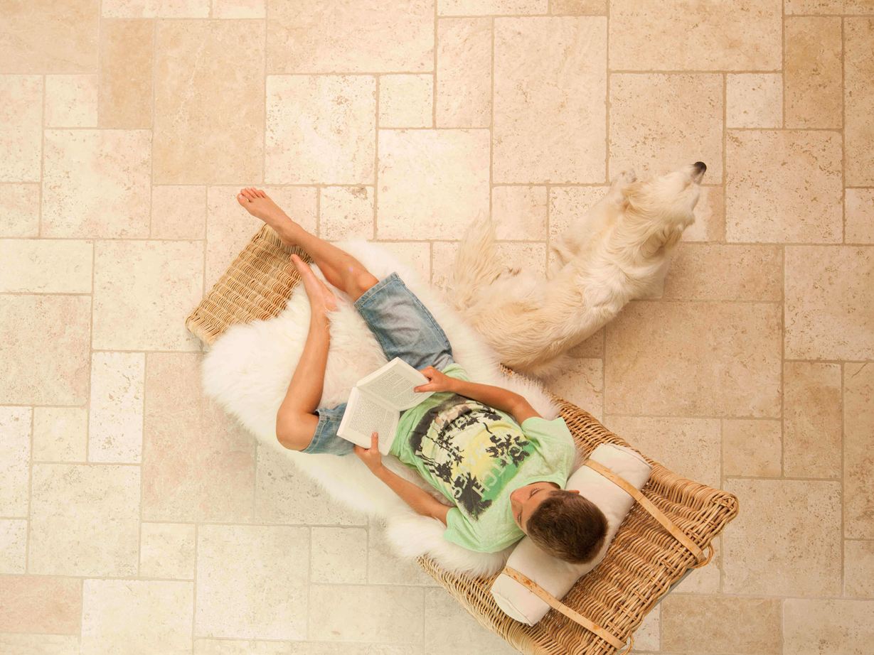Živý pocit z bydlení ve středomořském stylu Chlapec si čte na lehátku na světlých travertinových dlaždicích položených v římské vazbě