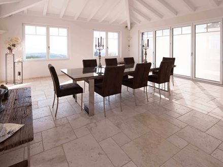 Jídelna s vysokým stropem, stolem a židlemi na travertinu Light v římské vazbě