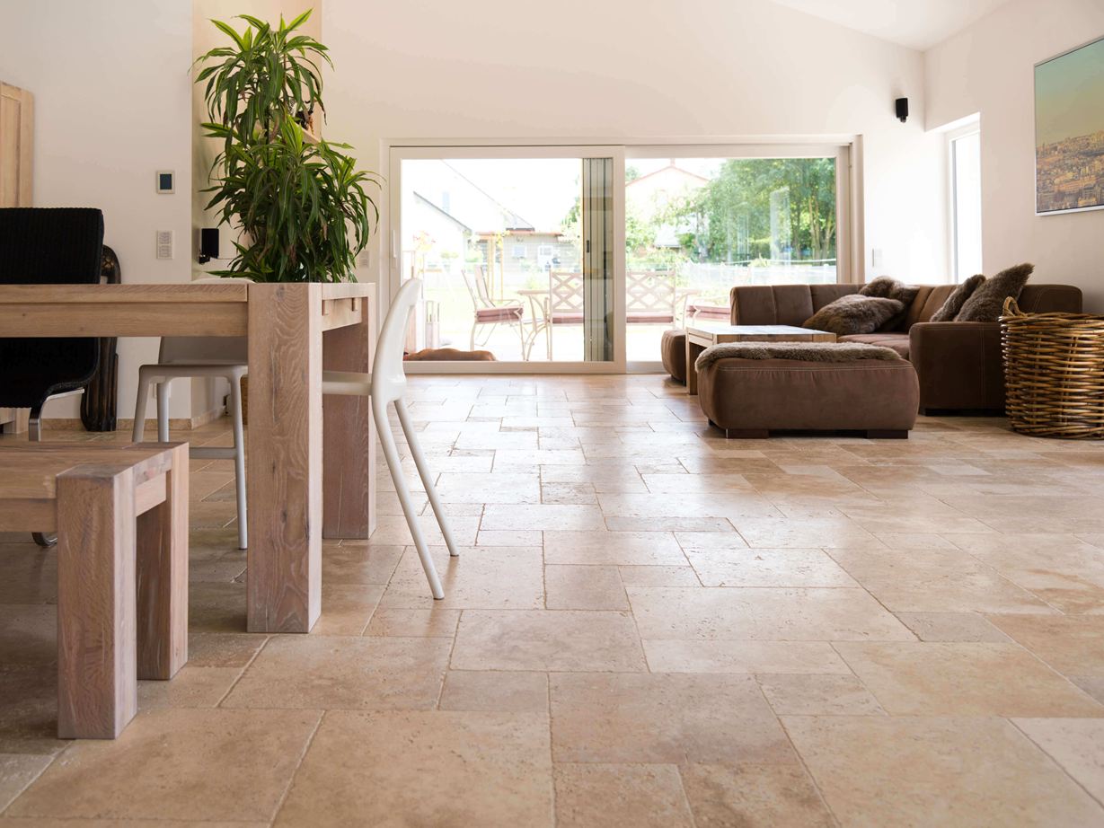 Obývací pokoj s hnědou pohovkou, bílými stěnami a dlaždicemi Medium Travertin v hnědobéžové barvě jako podlahou