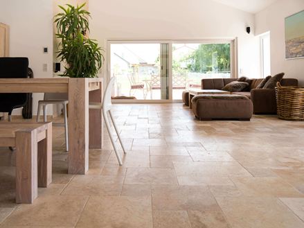 Obývací pokoj s hnědou pohovkou, bílými stěnami a dlaždicemi Medium Travertin v hnědobéžové barvě jako podlahou