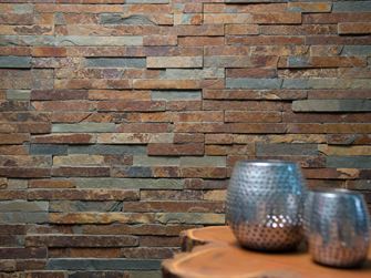 Dvě vázy na dřevěném stole před obkladem stěny z přírodní břidlice v jasných barevných odstínech.