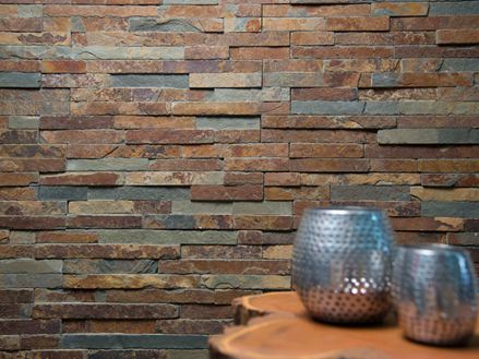 Dvě vázy na dřevěném stole před obkladem stěny z přírodní břidlice v jasných barevných odstínech.