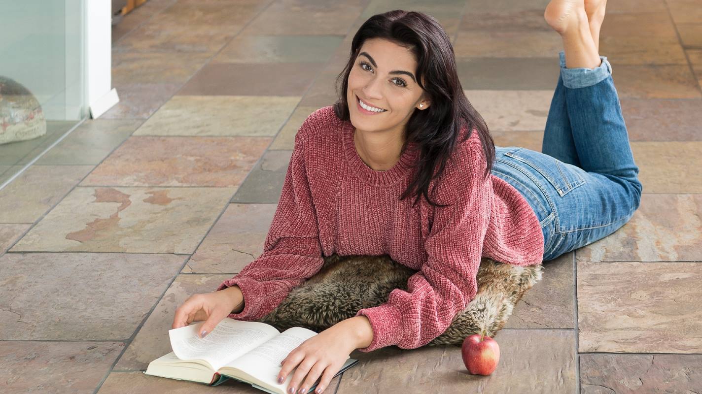 Žena ležící na břidlicové podlaze Peacock Multicolor a čtoucí knihu
