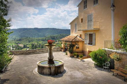 Kašna na náměstí vedle venkovského domu, v pozadí hory