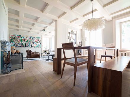 Moderní obývací pokoj a jídelna s vysokými bílými stropy, dřevěnou podlahou a moderním obrazem v pozadí