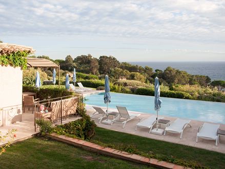 Bazén s bílými lehátky a travertinovými deskami s mořem v pozadí