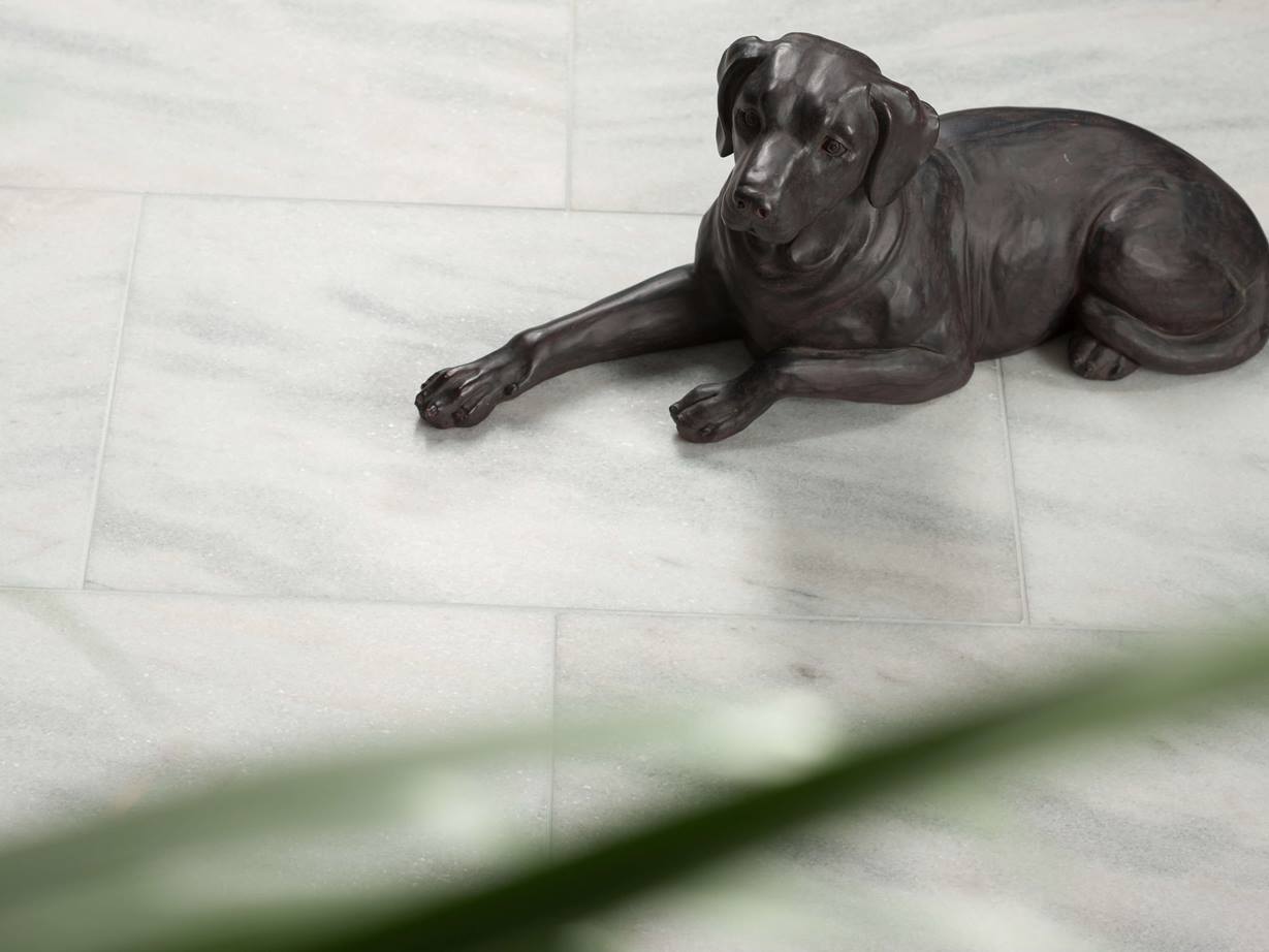 Porcelánová figurka ležícího psa broušená na mramorové dlaždici Calacatta