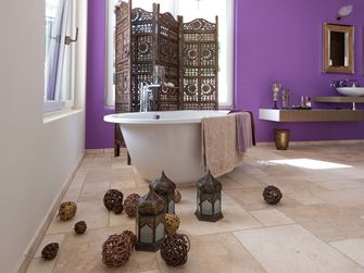 Dlaždice Travertin Light v koupelně s volně stojící vanou a fialovou stěnou v pozadí