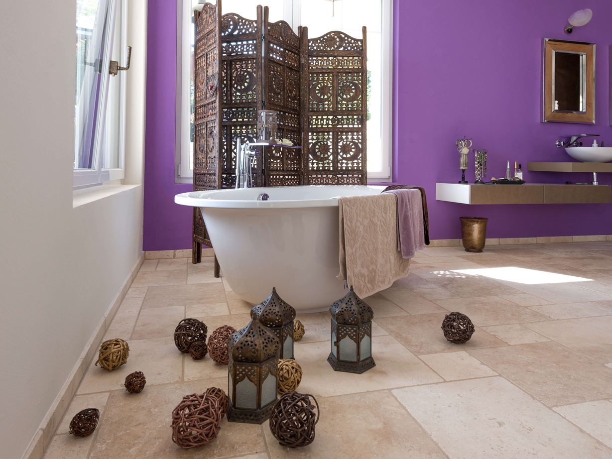 Dlaždice Travertin Light v koupelně s volně stojící vanou a fialovou stěnou v pozadí