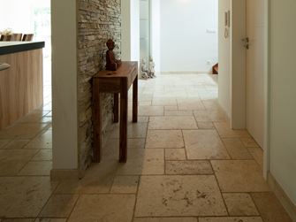 Chodba s podlahou ze světlé travertinové dlažby, malým dřevěným stolkem a obložením z přírodního kamene na jedné stěně.