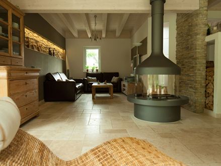 Obývací pokoj se samostatným krbem a posezením na světlé travertinové dlažbě, v popředí proutěné křeslo