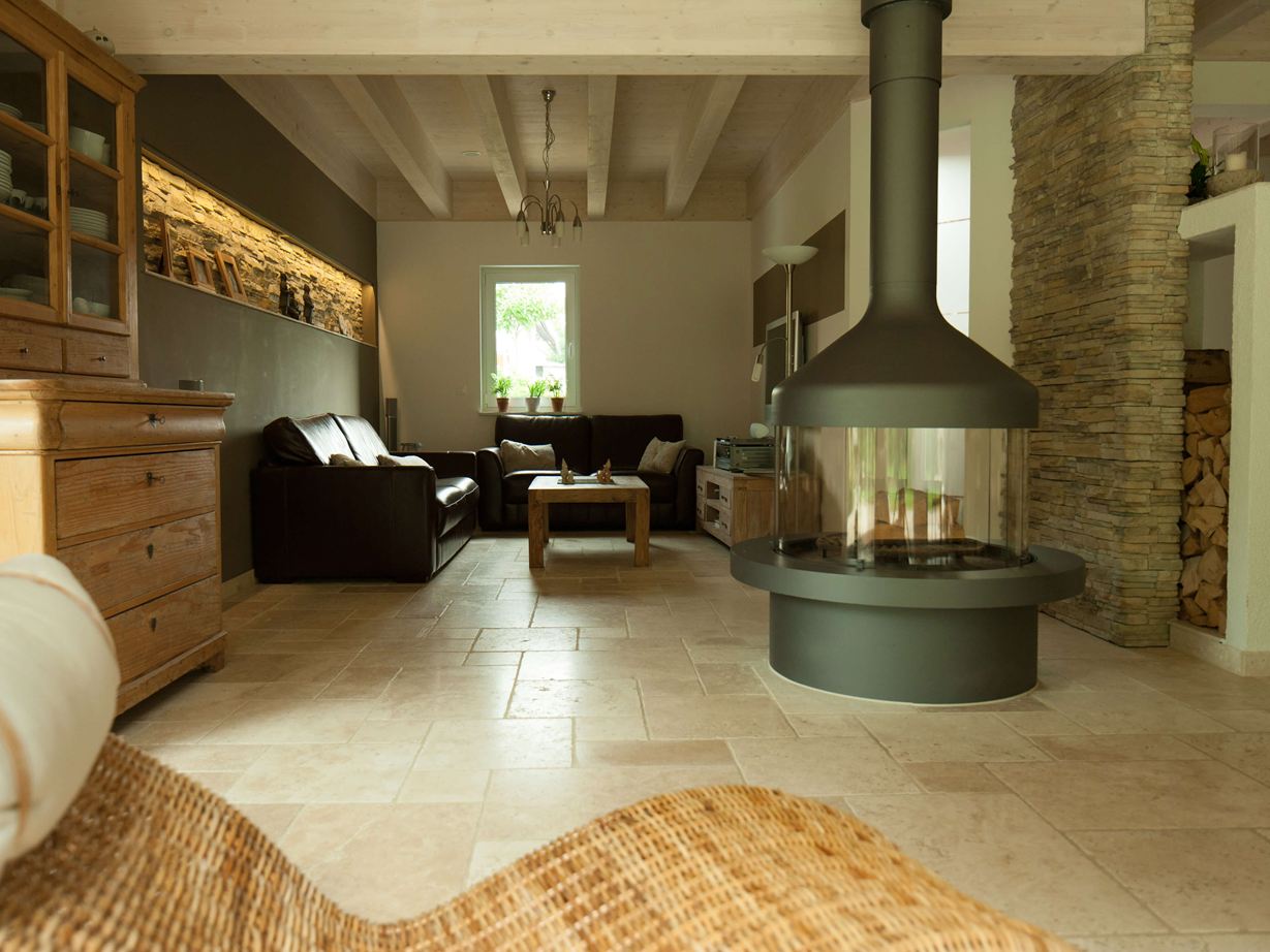 Obývací pokoj se samostatným krbem a posezením na světlé travertinové dlažbě, v popředí proutěné křeslo