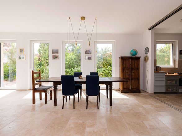 Světlá jídelna s dřevěným nábytkem a béžovou travertinovou dlažbou jako podlahou