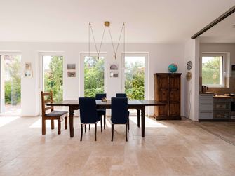 Světlá jídelna s dřevěným nábytkem a béžovou travertinovou dlažbou jako podlahou