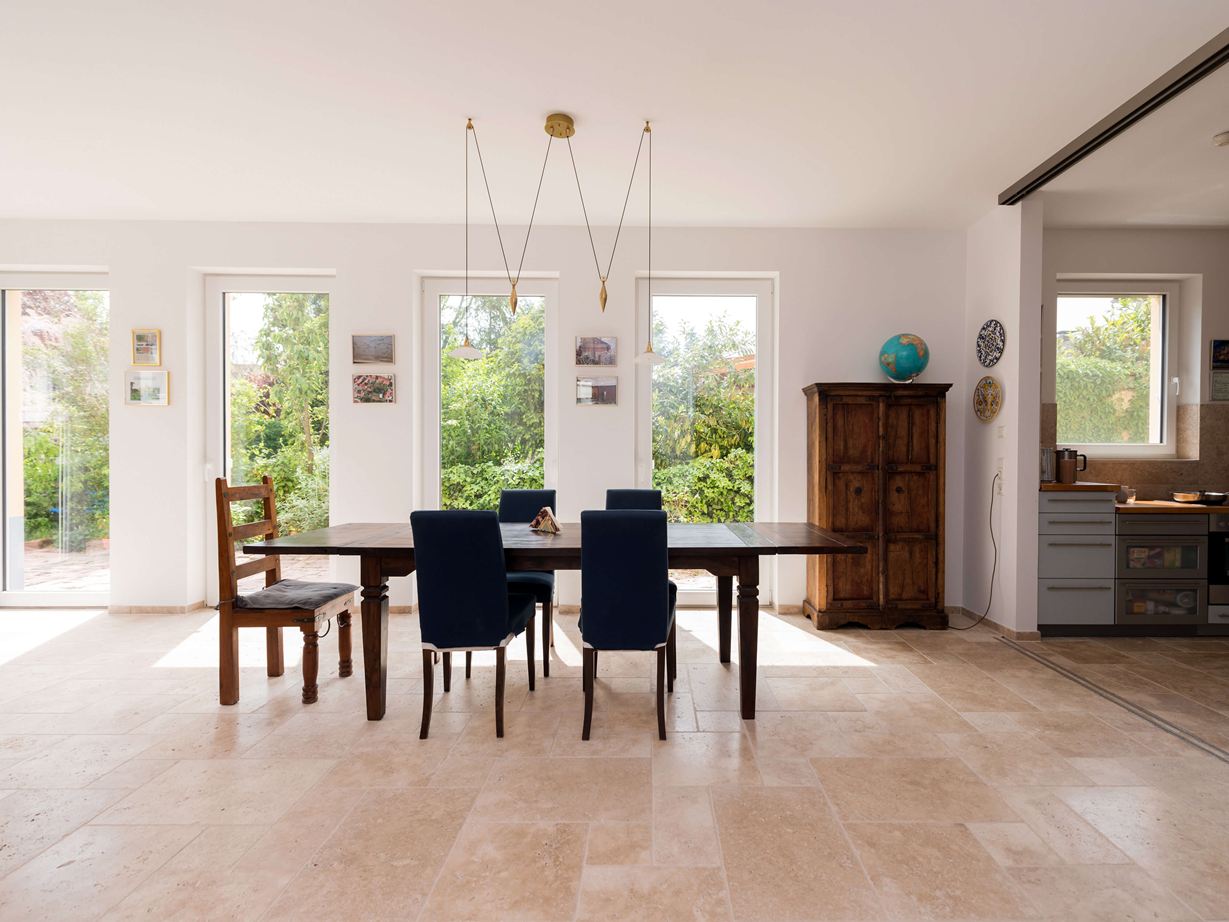 Světlá jídelna s dřevěným nábytkem a béžovou travertinovou dlažbou jako podlahou