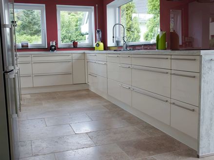 Zákaznická fotografie kuchyně s bílým nábytkem, červenými stěnami a béžovo-hnědými travertinovými dlaždicemi