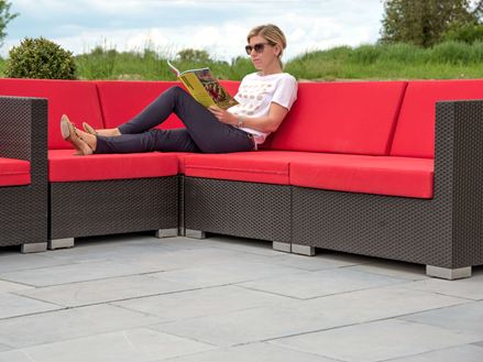 Žena sedící na moderním gauči s červenými polštáři na terase z modrého kamene