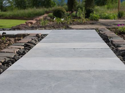 Modrokamenné desky jako zahradní cesta se záhony květin a zeleným trávníkem v pozadí