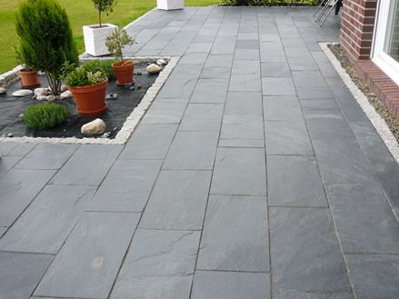 Terasa s rostlinami v květináčích a Black Rustic břidlice jako podlahová krytina, vpravo je vidět cihlová zeď domu.