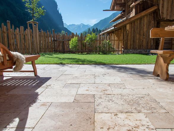 Podlaha terasy s travertinovým Rustic a dřevěným nábytkem, trávník v pozadí a výhled na hory