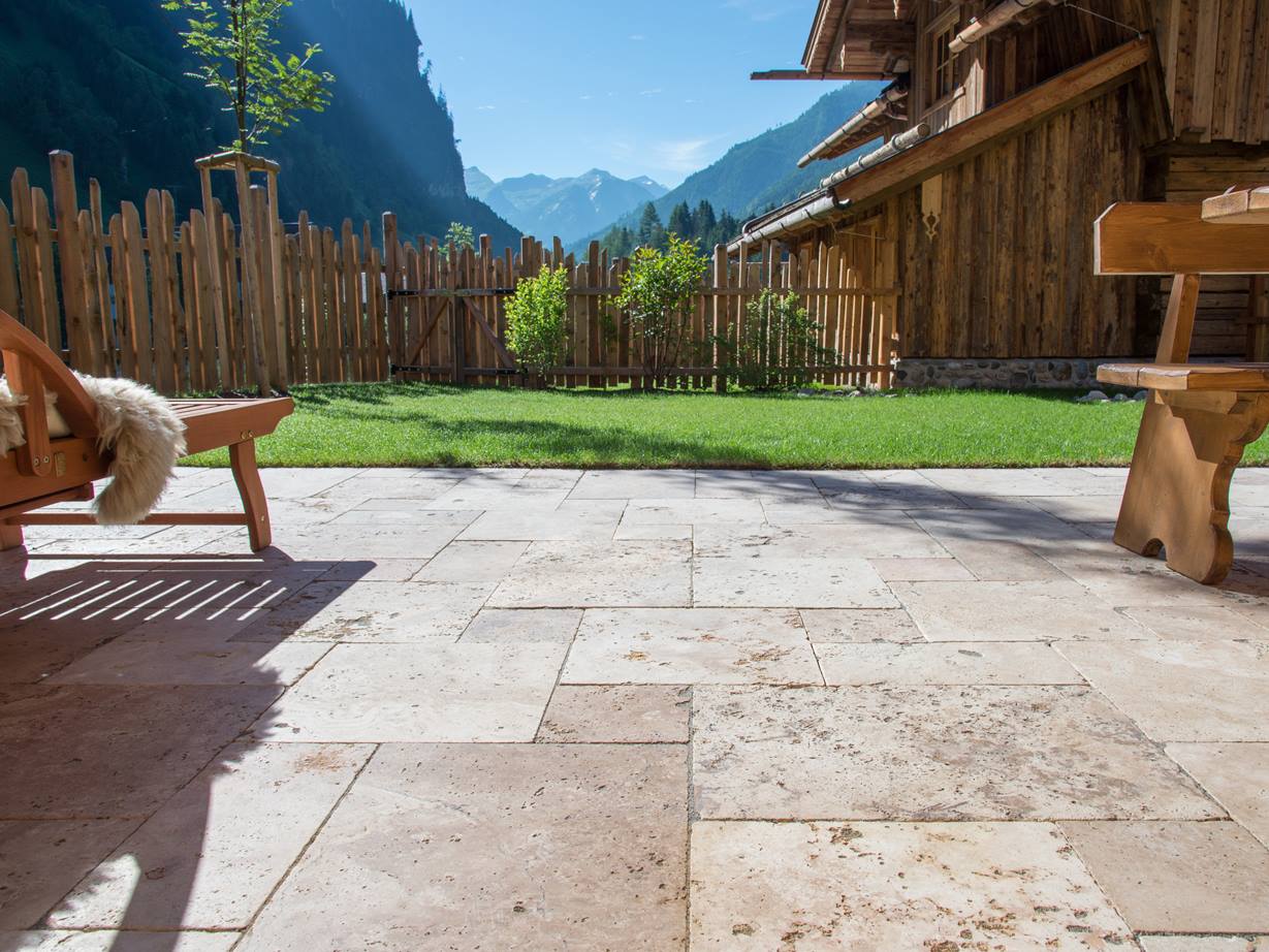 Podlaha terasy s travertinovým Rustic a dřevěným nábytkem, trávník v pozadí a výhled na hory