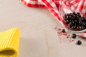 Žlutá utěrka, červená utěrka a skleněná miska s bobulemi vyklopená na přírodní kámen.