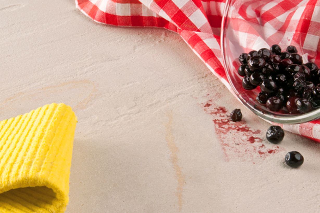 Žlutá utěrka, červená utěrka a skleněná miska s bobulemi vyklopená na přírodní kámen.